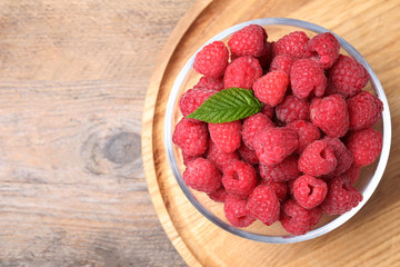 Delicious fresh ripe raspberries in bowl on wooden table, top view. Space for text