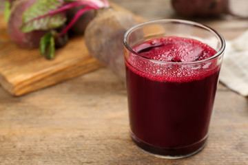 Freshly made beet juice in glass on wooden table. Space for text