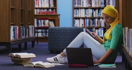Asian female student wearing a yellow hijab sitting and using laptop - Powered by Adobe