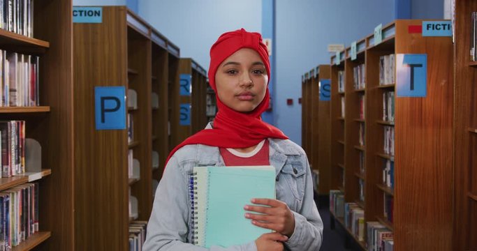 Portrait of a smiling Asian female student wearing a red hijab studying in a library