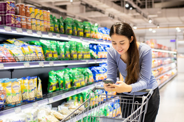 Beautiful young Asian woman pushing cart for shopping in a supermarket. Shopping supermarket concept.