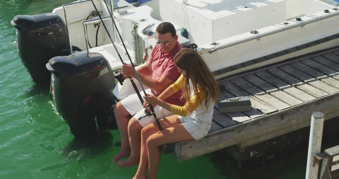 Side view of a Caucasian man and his teenage daughter fishing harbor side 
