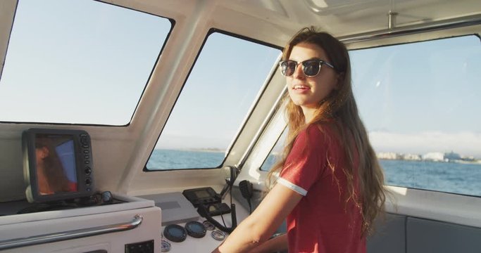 Side view of a teenage Caucasian girl driving a boat and looking at camera