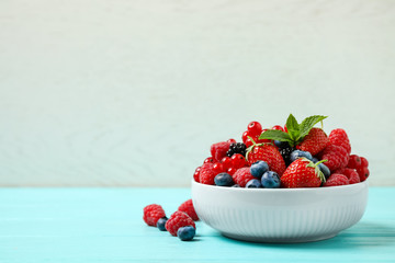 Mix of different fresh berries and mint in bowl on light blue wooden table. Space for text