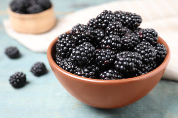 Fresh ripe blackberries in bowl on blue wooden table, closeup