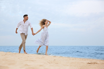 Fototapeta na wymiar Happy couple running on beach, space for text. Romantic walk
