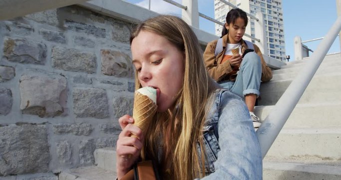 Side view of a Caucasian and a mixed race girl eating ice cream sitting on stair