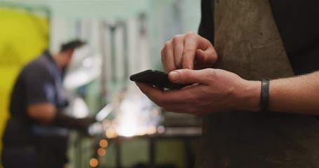 Caucasian male factory worker at a factory standing in a workshop, using his smartphone