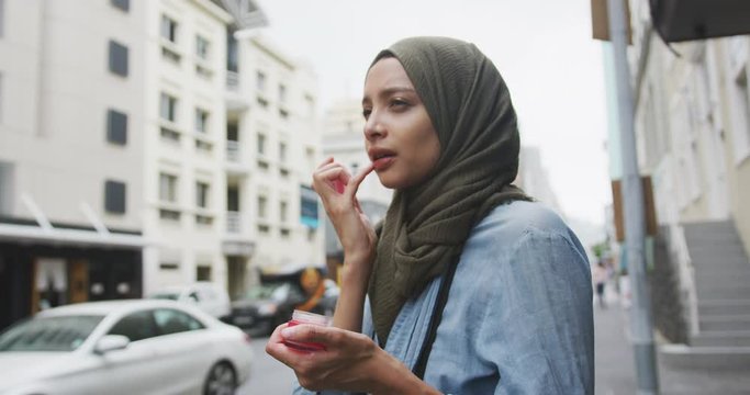 Woman wearing hijab putting lipstick in the street 