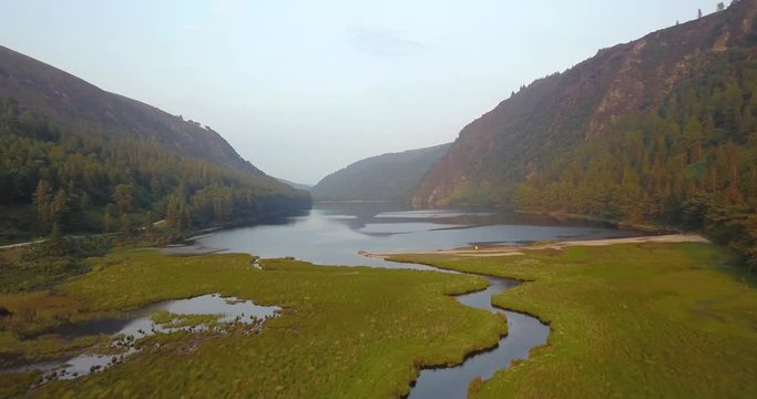 Aerial shot following river with Glendalough Upper Lake in the background in Wicklow National Park, Ireland