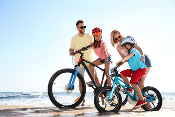 Fototapeta premium Happy parents teaching children to ride bicycles on sandy beach near sea