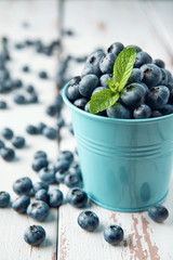 Blue bucket with blueberry and mint leaves on white Provence style wooden table. Close-up.
