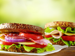 Sandwiches with ham, bacon, tomato, cucumber, cheese, and herbs on green nature background.