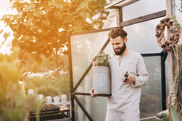 happy bearded male nursery worker trimming plants in greenhouse