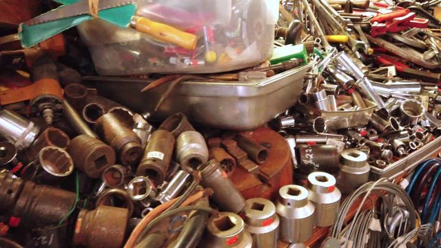 Hoarder sells many tools, parts, gadgets, junk and bargain items stacked and piled together on messy and crowded tables for sale in thrift store at flea market, handheld close up pan right