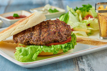 Delicious grilled  burger on white plate on wooden table.  with sauces, french fries and salads.