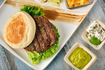 Delicious grilled  burger on white plate on wooden table.  with sauces, french fries and salads.