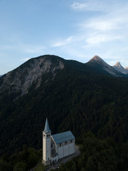 Fototapeta na wymiar Aerial view of tyrolean church in Alps mountains Dolomites Italy, South Tyrol, Europe. Early morning sunrise, blue sky, high mountain range, clouds. Summer.