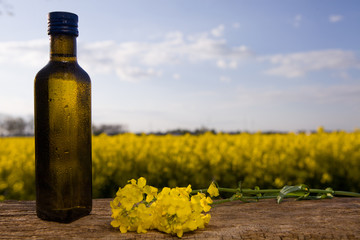 Rapeseed oil in bottles on wooden table on background flowering rape field.