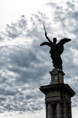 Fototapeta premium Statue of an angel in Rome with sword and clouds background with sun rays as divine light
