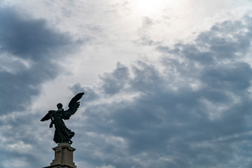 Statue of an angel in Rome and clouds background with sun rays as divine light