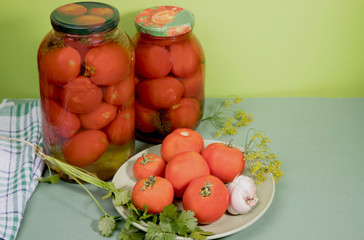 Marinated tomatoes in jars . Fresh tomatoes with garlic and herbs are on a plate. Horizontal orientation.