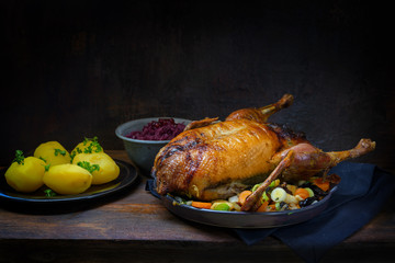 Roasted duck with potatoes and red cabbage, a festive meal on a rustic wooden table, dark brown background with copy space, selected focus, narrow depth of field