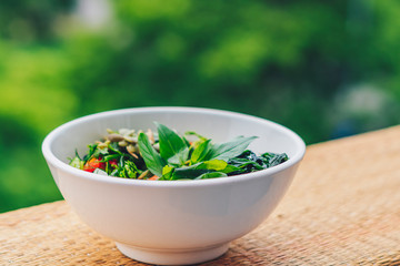 Beautiful raw vegan salad from green leaves mix vegetables in white plate. Cooking recipe Blended tomato carrot cauliflower, cut parsley cilantro dill greenery cucumber, basil pumpkin seed, seaweed