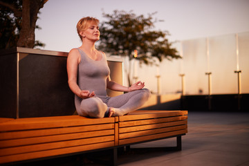 Middle age caucasian woman practicing yoga outdoors in city during beautiful sunset at summer. 