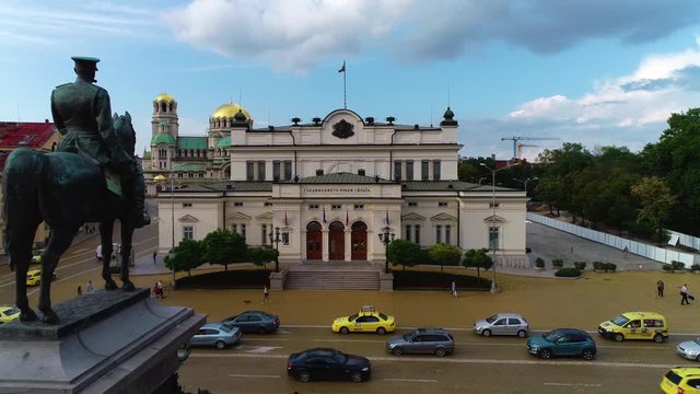 Drone shot of statue of horse man  in the street next to a big urban  building  and view of city transport 