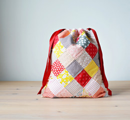Colorful patchwork drawstring bag on wooden table and white wall