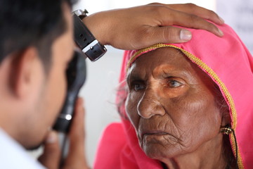 Old Indian woman in pink mantilla from Rajasthan getting eyes tested. Eye camp. Eye patient. Weak eyesight. Eye Health. Eye examination by doctor. Healthcare to elderly. 