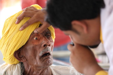 Old Indian man in Yellow turban from Rajasthan getting eyes tested. Eye camp. Eye patient. Weak eyesight. Eye Health. Eye examination by doctor. Healthcare to elderly. 