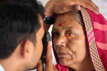 Old Indian woman in pink mantilla from Rajasthan getting eyes tested. Eye camp. Eye patient. Weak eyesight. Eye Health. Eye examination by doctor. Healthcare to elderly.
