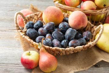 Assortment of fruits in a basket on the table. There are a lot of different raw fruits in the basket. Plums, peaches, apples and pears on the table. Healthy food concept	