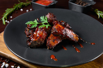 Spicy hot grilled spare ribs from a summer BBQ served with a hot chili pepper and fresh tomatoes on an old vintage wooden board.