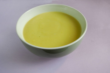 green plate with cream soup of zucchini, potatoes, cream, onions on a purple background of side view . cooking gluten-free food at home