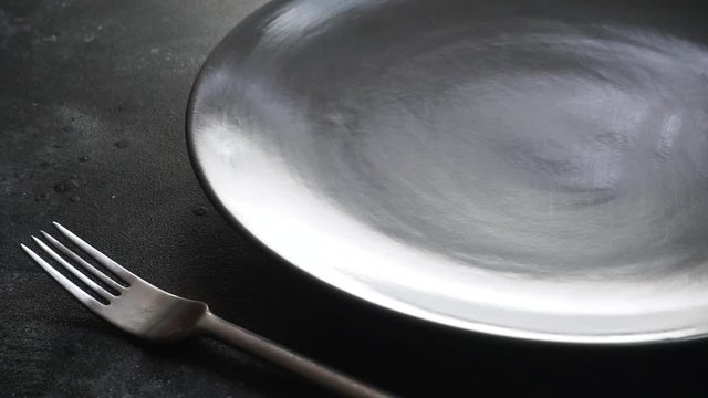 Empty plate on the table. Empty gray dinner plate and fork set on a table in a restaurant or kitchen.
