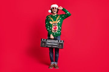Full length body size view of attractive cheerful guy wearing Santa hat carrying cassette tape...