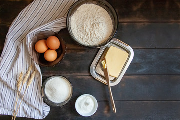 Baking ingredients for shortcrust pastry: butter, flour, eggs, sour cream, a towel on a wooden background. Flatley top view