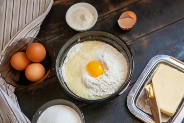Baking ingredients for shortcrust pastry: butter, flour, eggs, sour cream, a towel on a wooden background. Flatley top view