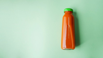 Nutritious detox carrot or pumpkin juice in glass bottle. Alkaline diet concept. Organic vegetarian drink on green background. Healthy eating. Flat lay, copy space for text