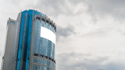 Obraz premium Daylight, overcast. Consumerism, mockup, background, isolated white screen, copyspace concept. Mock up image - blank white billboard or large advertising display on tall building, glass skyscraper