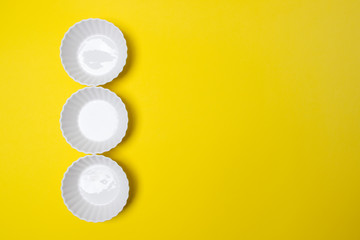 three empty white plate on yellow colored paper background with copy space