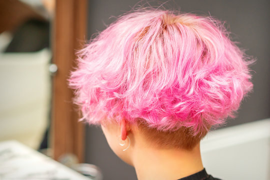 Back view of pink hairstyle of young woman after dyeing hair and making highlights in beauty salon