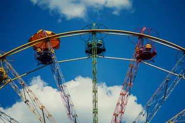 Booths of a multi-colored carousel against a blue sky with clouds