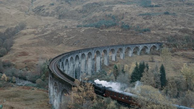Jacobite steam train passing the Glenfinnan Viaduct with the mountains in the background in Scotland. Train used in the Harry Potter movie.