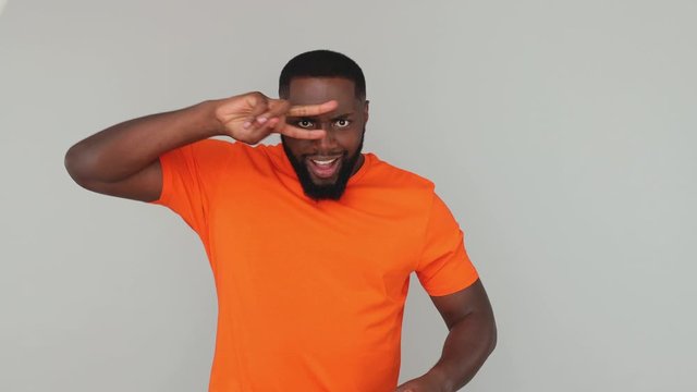 Young bearded african american guy 20s in orange basic casual t-shirt look at camera dancing fooling around having fun expressive gesticulating with hands isolated on grey color gray background studio