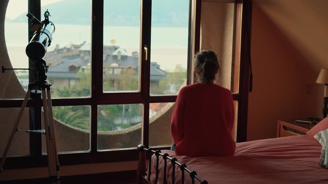 Girl looking through the window at sunset in her dormer room. Hobbie while you have to be locked up at home. Confinement, being at home.