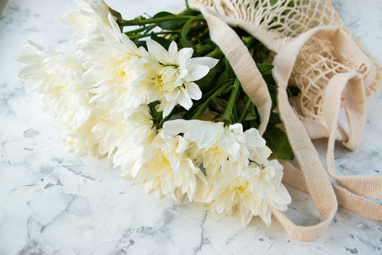 White chrysanthemum flowers in a cotton mesh bag on a light background. Copy space for your text.